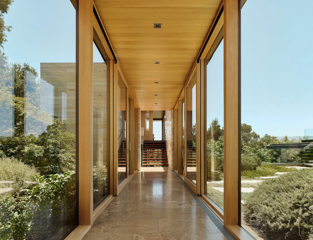 Hallway with floor-to-ceiling wood-framed windows and wooden ceiling, looking toward stairs at the end.