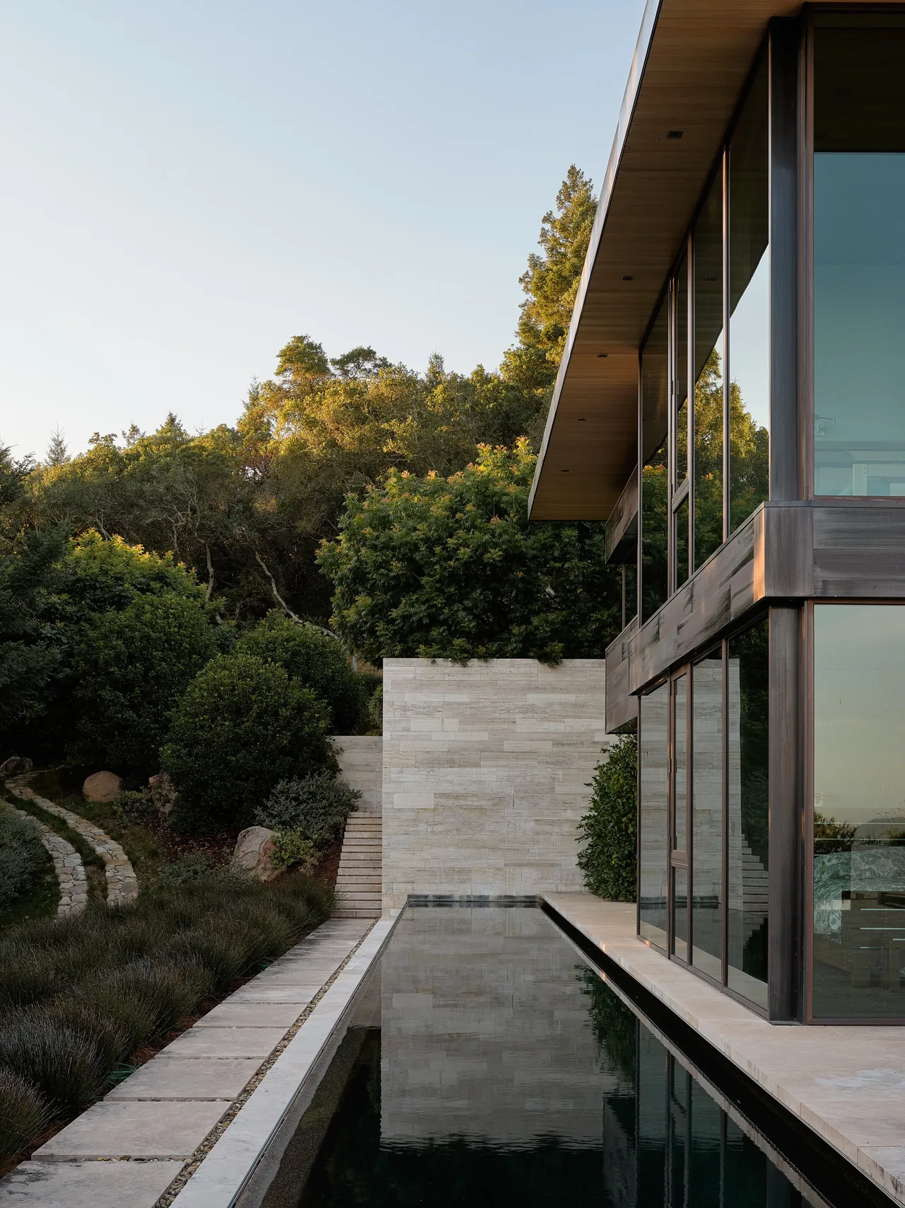 Modern home exterior with large glass walls, wood soffit, and a reflecting pool next to manicured landscaping.