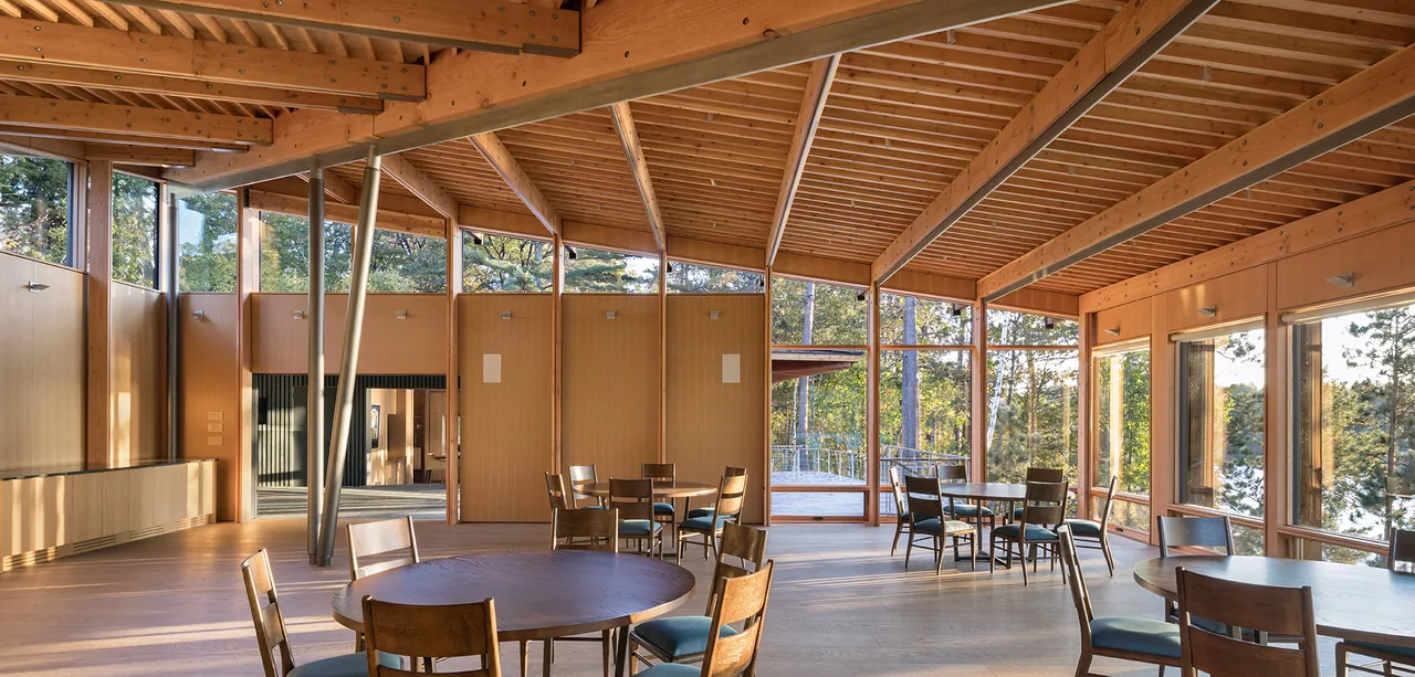 Interior of The Nest features exposed wooden beams, wood panel ceilings, and large wood-framed windows overlooking forest surroundings.