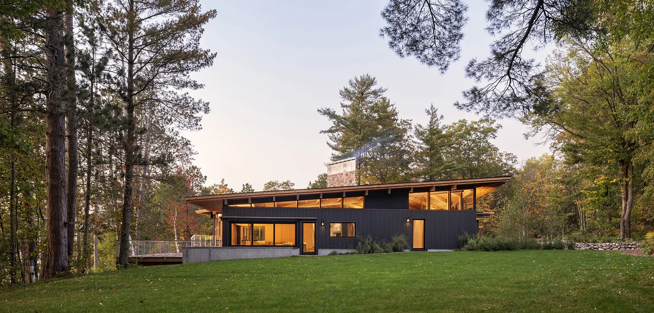 The Nest by SALA Architects features a sloped roof and large windows nestled in a forested setting.
