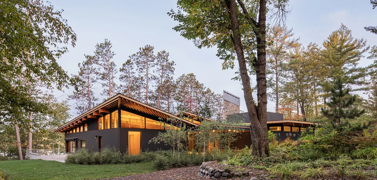 Modern residential exterior with wood beam ceiling and large windows in a forest setting.