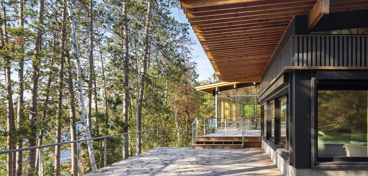 The Nest features vertical siding and exposed wood panel ceiling on the large outdoor deck with forest views.