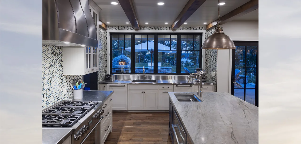 Kitchen of Tall Tree Lodge features stainless steel appliances, white cabinets, gray marble island countertop, and black framed windows.