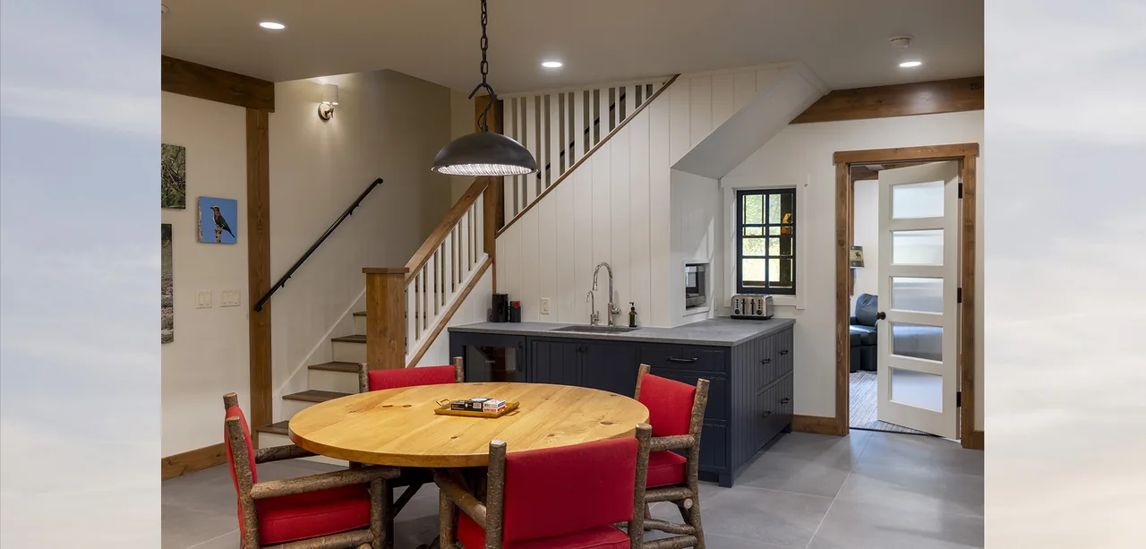 The kitchen features a round wood table with red cushioned chairs and a staircase with wood trim and white paneling under the stairs.