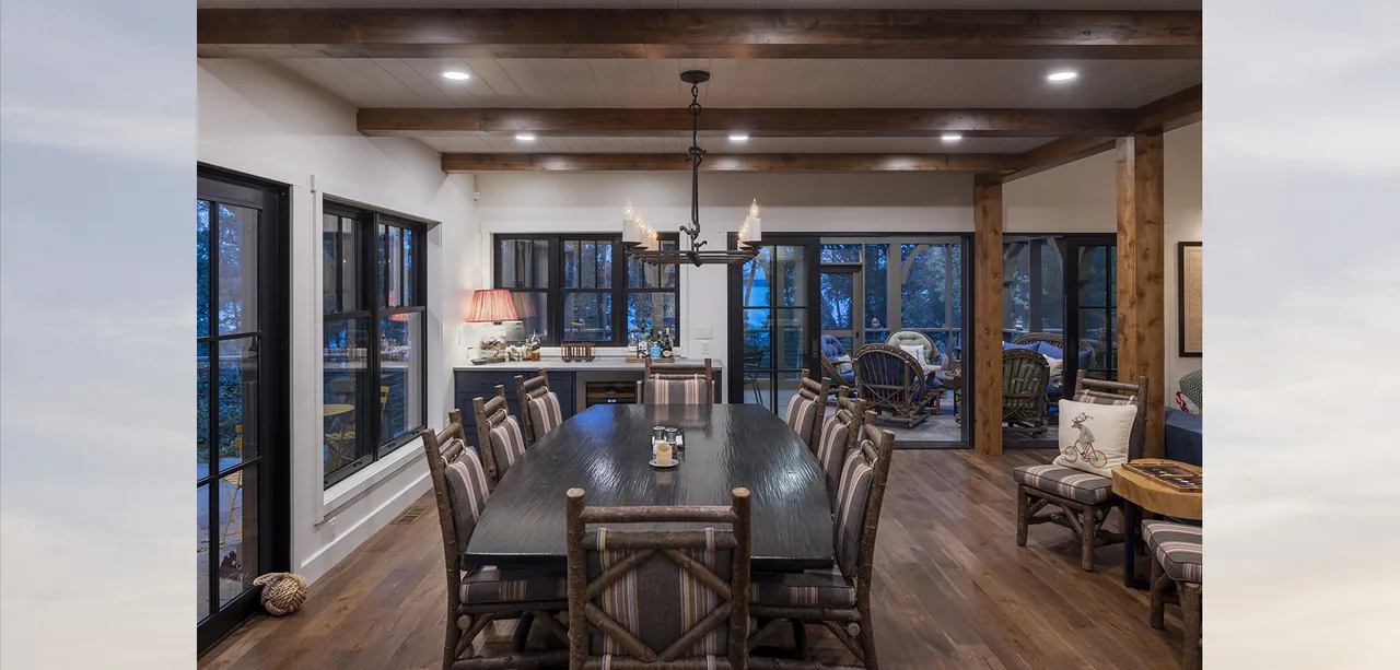 Dining area with exposed wood beams, a large dark wood table, and black-framed windows surrounding it