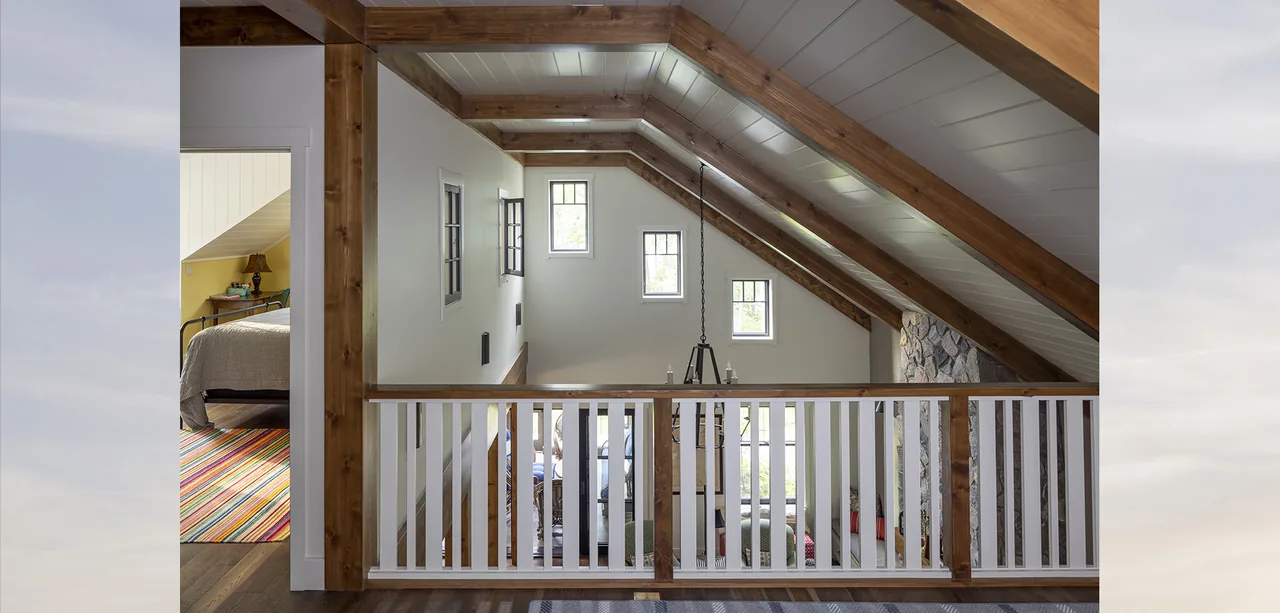 Loft hallway with exposed wood beams and vertical railing above a living space in the Tall Tree Lodge project.