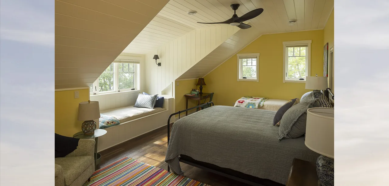 The bedroom in Tall Tree Lodge features a window seat beneath a sloped ceiling and multiple small windows.