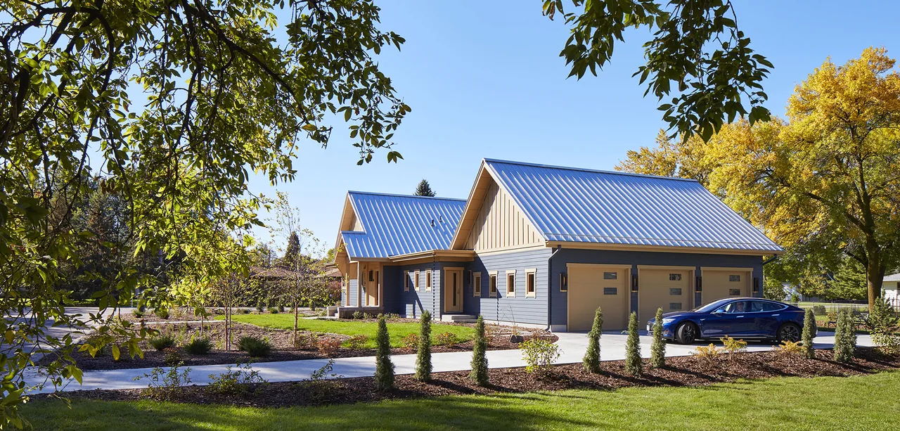 Modern house with blue siding and metal gable roofs, including a three-car garage with beige doors.