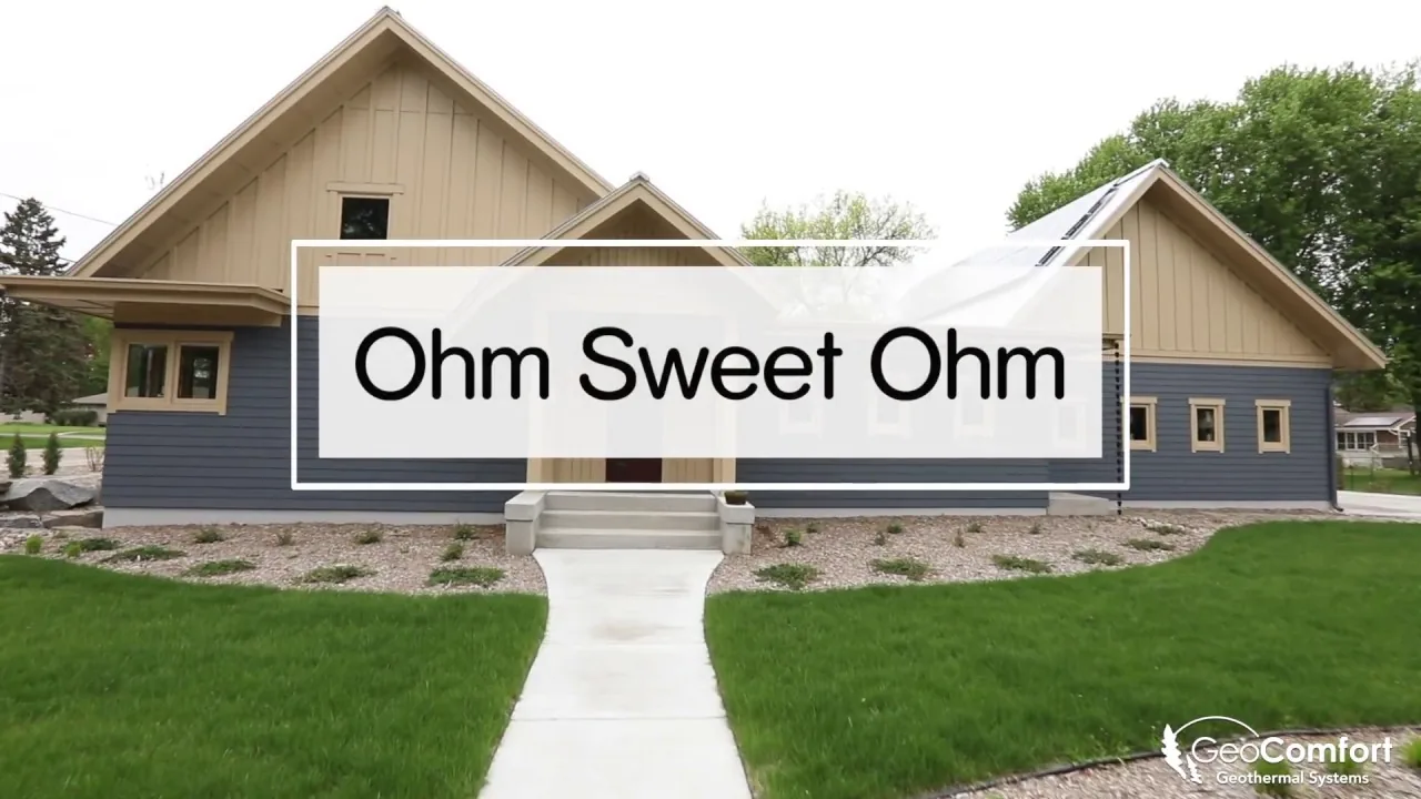 Front exterior of Ohm Sweet Ohm house shows mixed siding and a concrete path leading to the entrance with landscaping of small plants and stone beds.