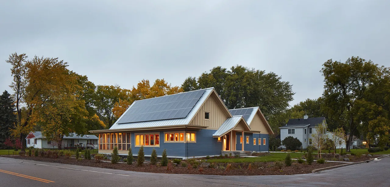 Ohm Sweet Ohm features a gable roof with solar panels and illuminated windows in a residential neighborhood.
