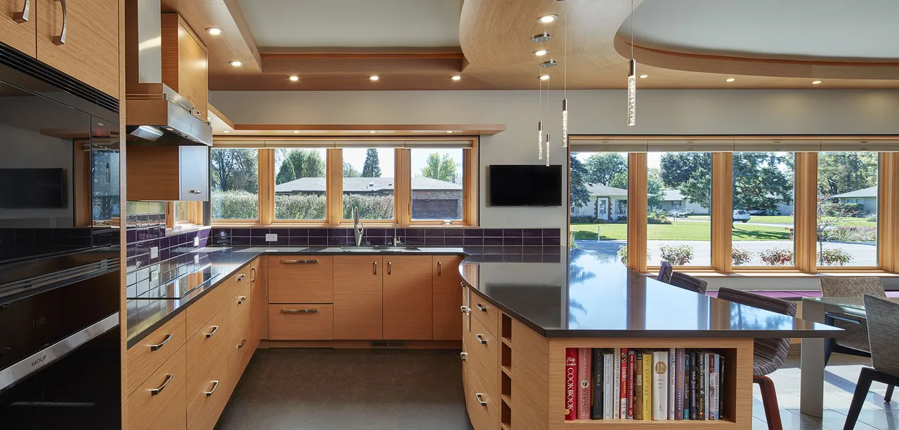 Bright kitchen features wood cabinetry, black countertops, and multiple small windows providing natural light to the space.