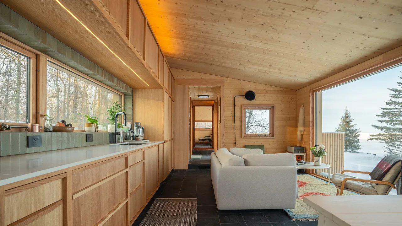 Warroad CLT House features wood-paneled interiors and large picture windows overlooking a snowy landscape.