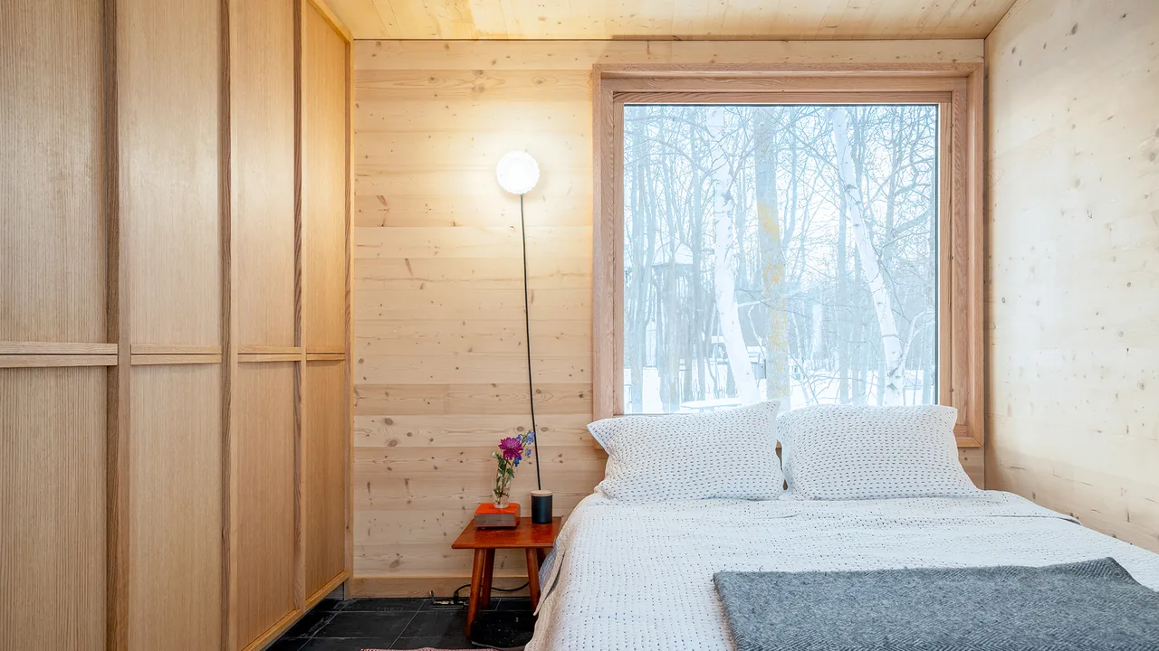 Bedroom with wood-panel walls and ceiling and a large window overlooking a snowy landscape.