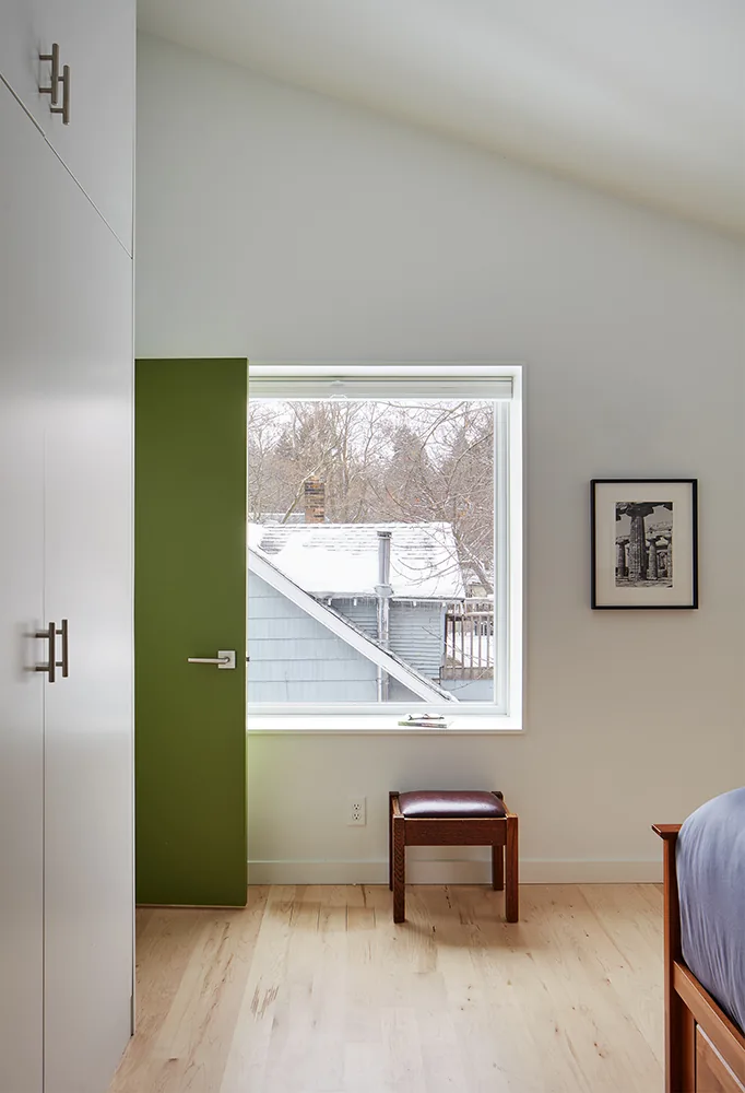 Bedroom view with green interior door open beside a window, showing a portion of a bed and a small bench under the window.