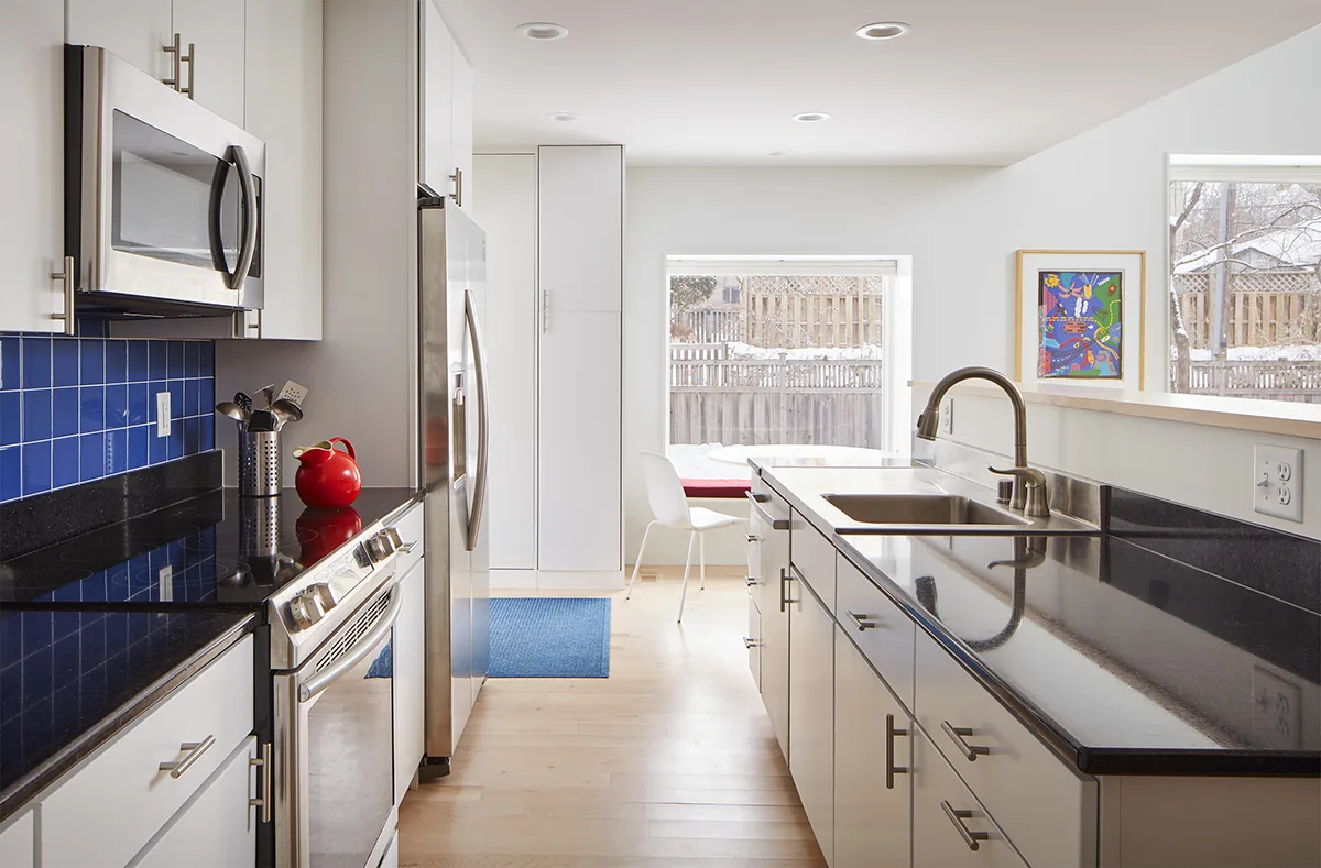 The kitchen features white cabinets, black granite countertops, and a blue tile backsplash, with views of a snowy backyard through large windows.