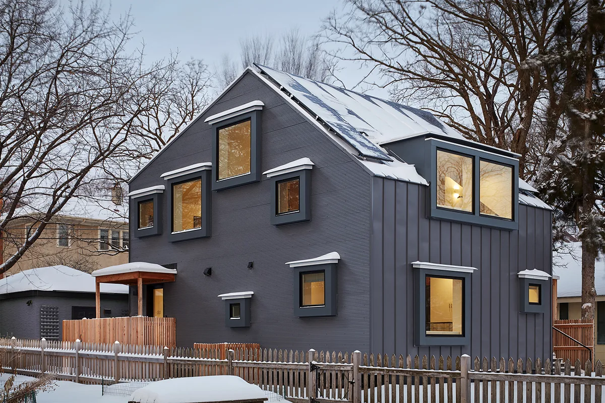 Modern dark gray two-story house with many square windows and a snowy roof.