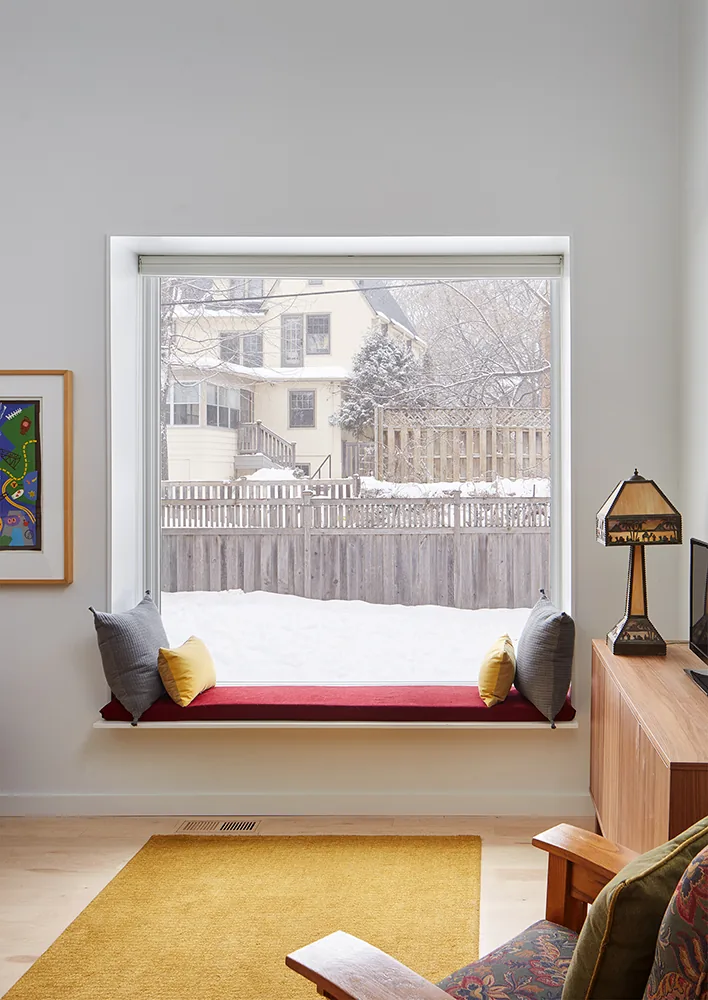 Large picture window with a built-in bench seat in front of a snowy backyard and wooden fences.