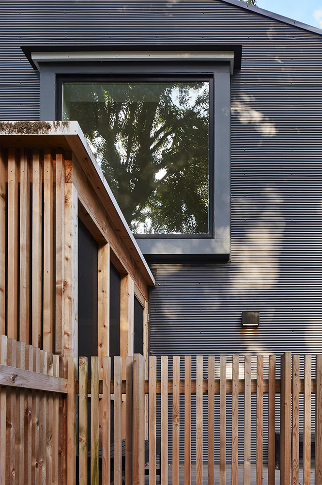 Detail of Electric Bungalow exterior with black metal siding, wood picket fence, and large window.