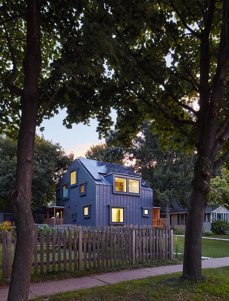 Modern Electric Bungalow with flat window frames and solar panels on the roof, surrounded by a lush yard and wooden picket fence.
