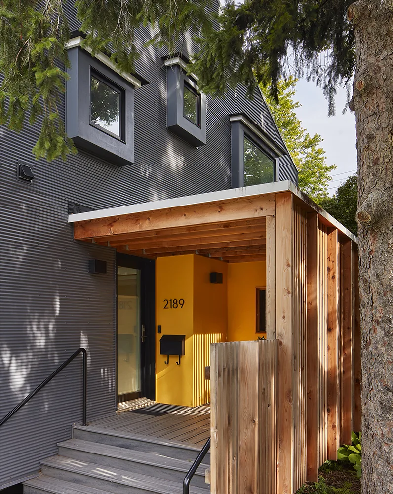 The Electric Bungalow features a yellow entry alcove under a wood pergola with black-framed windows above.