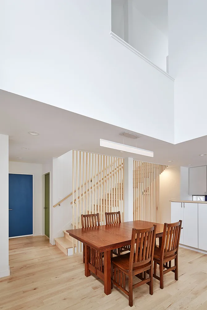 Dining area with a wooden table and chairs adjacent to a vertical wood slat staircase and a blue door in the background.