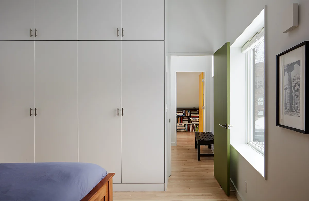 Bedroom with floor-to-ceiling white cabinets and a green door opening to a hallway with built-in bookshelves.