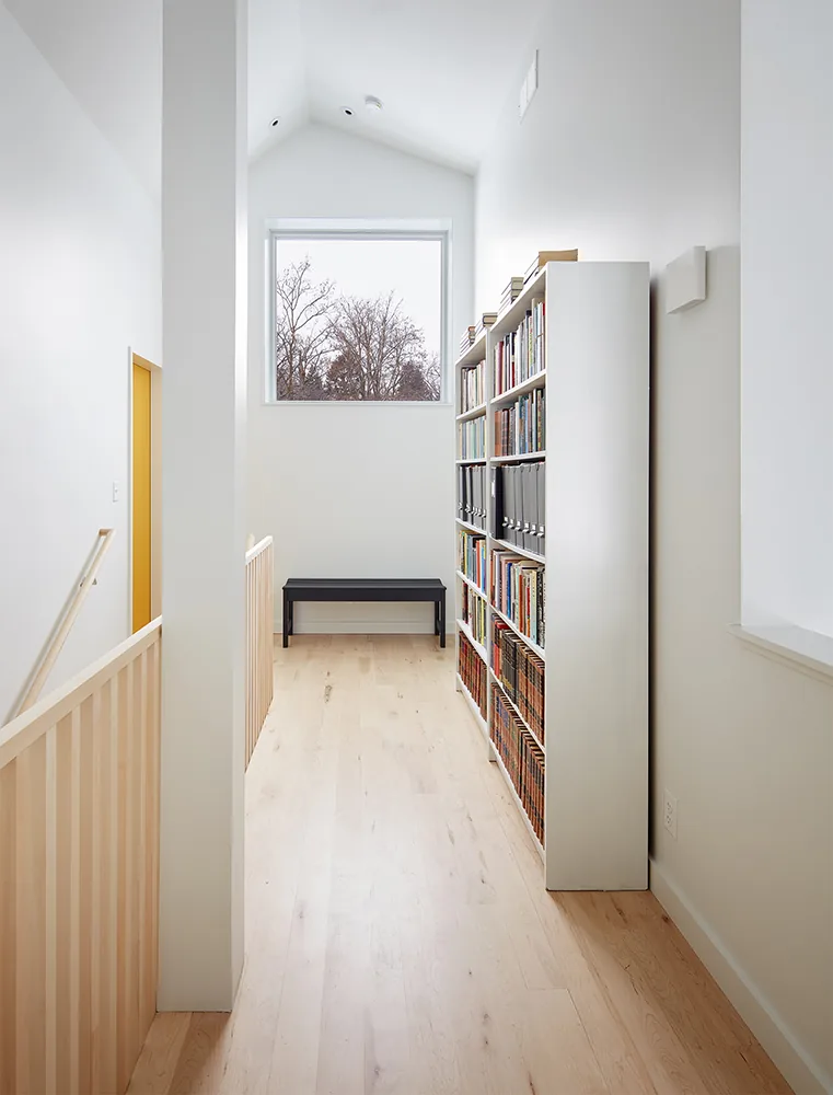Hallway with vaulted ceiling, natural light from a large window, wooden floor, and a bookshelf along one wall.