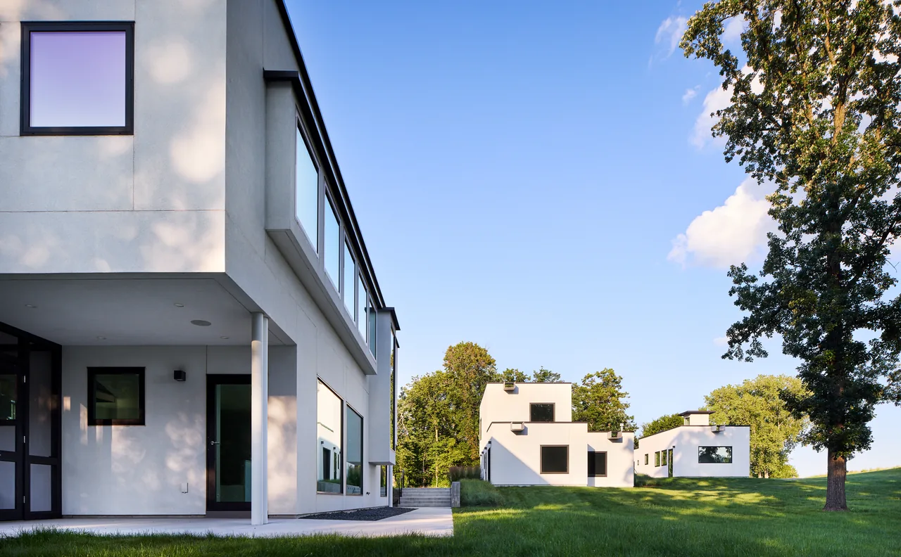 Bauhaus Farm features rectangular white buildings with flat roofs and black window frames set in a grassy field at evening light.