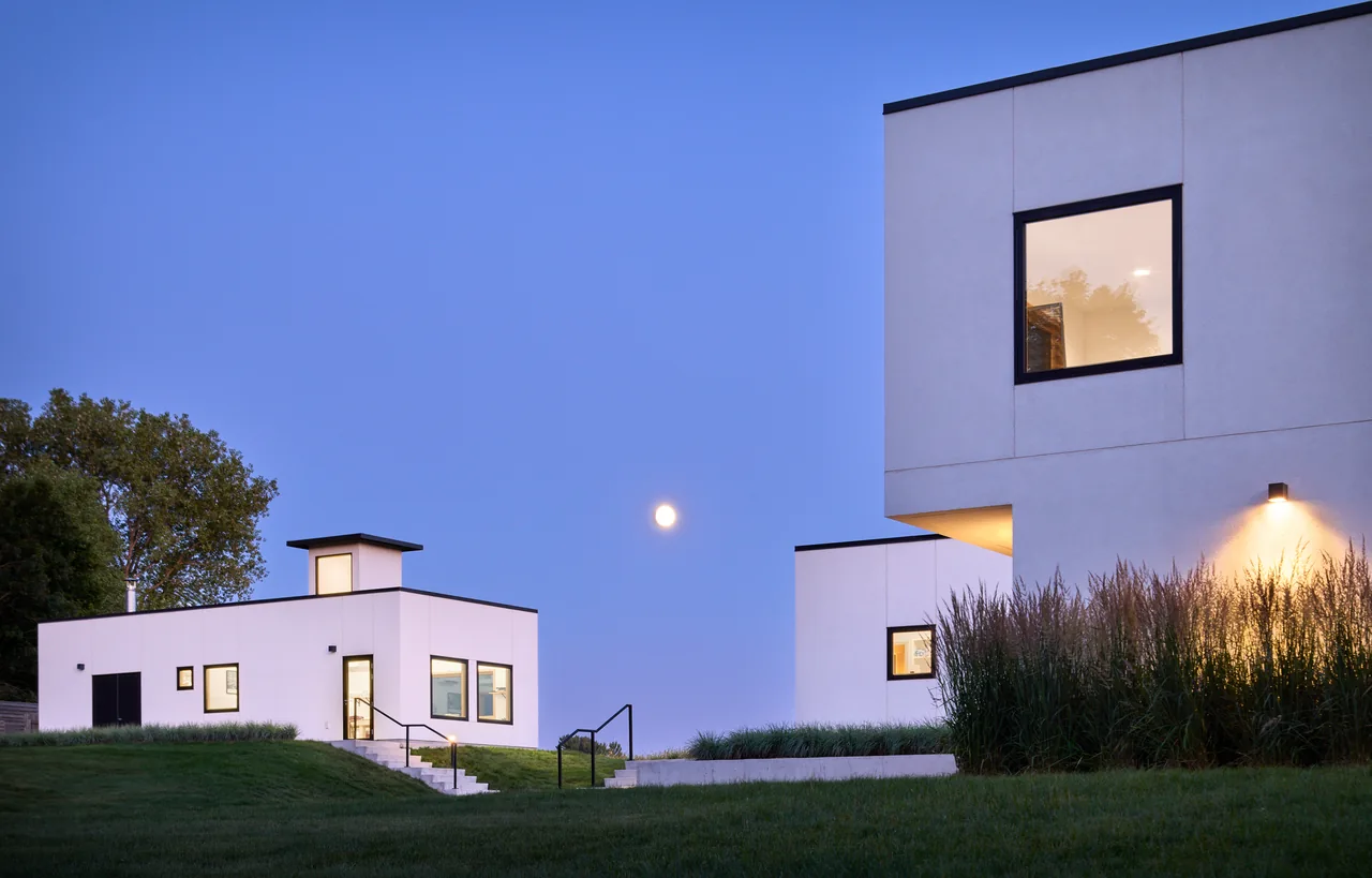 The Bauhaus Farm showcases minimalist cubic forms with white stucco walls and flat black-trimmed roofs at dusk.