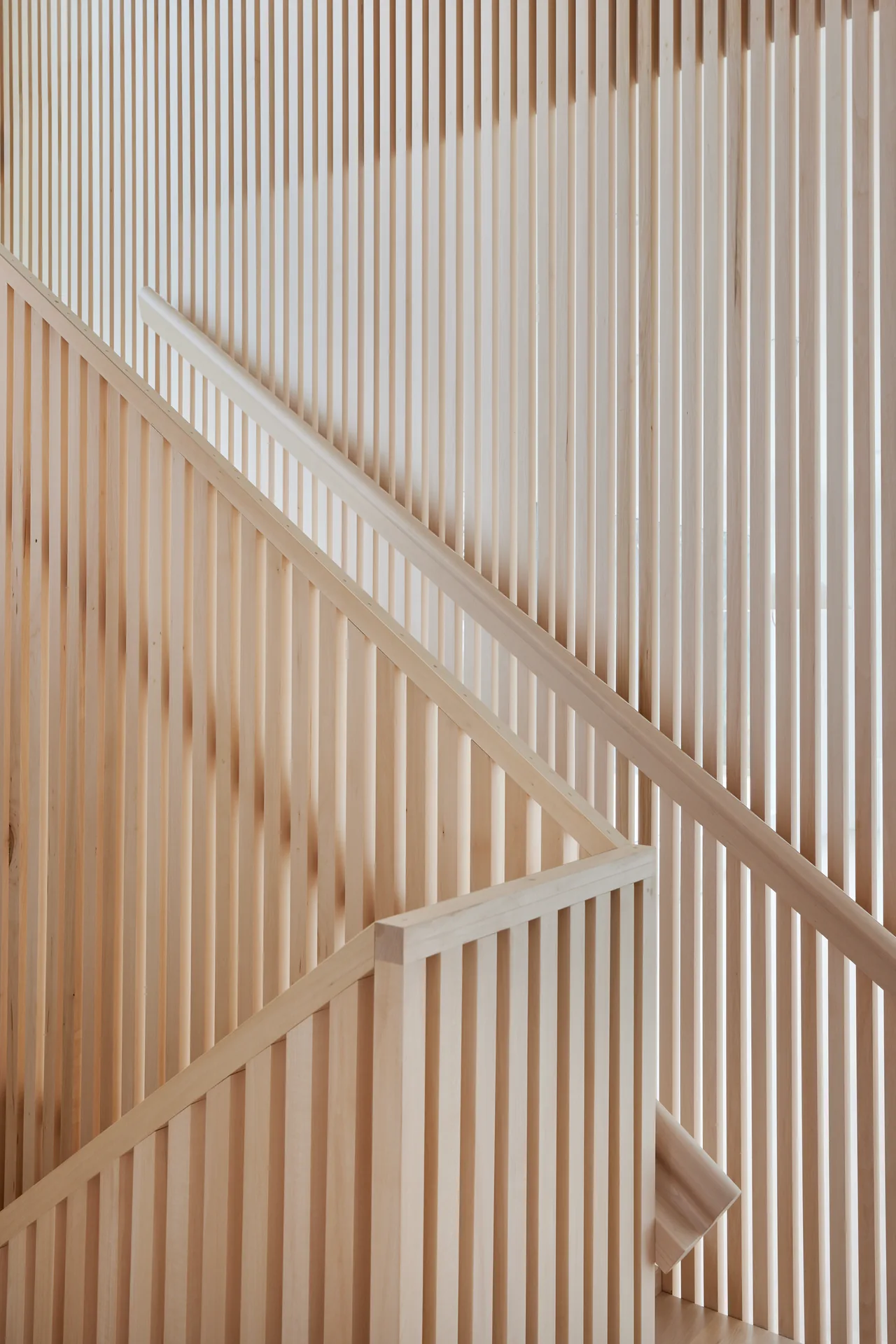 Close-up of a staircase featuring vertical light wood slats as railing and wall design elements.