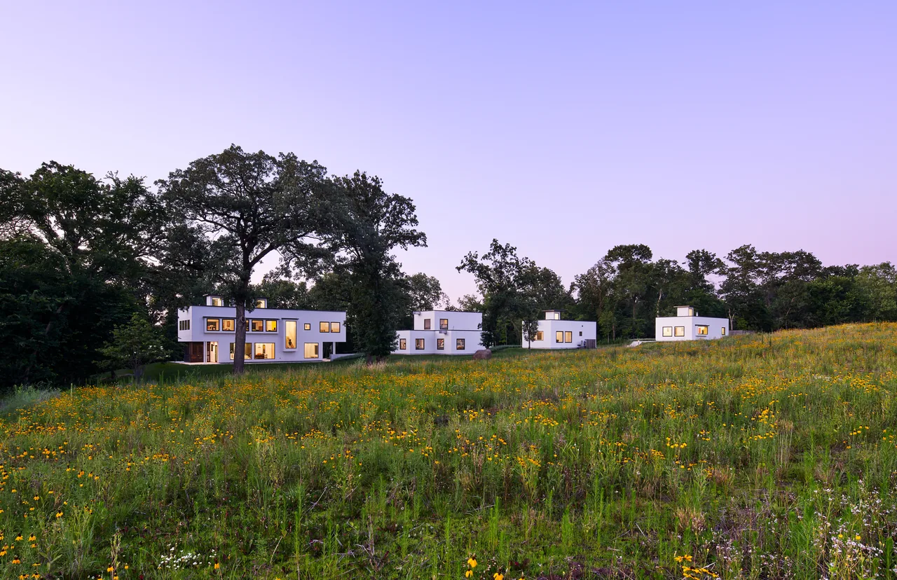 Bauhaus Farm features four white modern buildings with flat roofs set on a grassy landscape with surrounding trees.