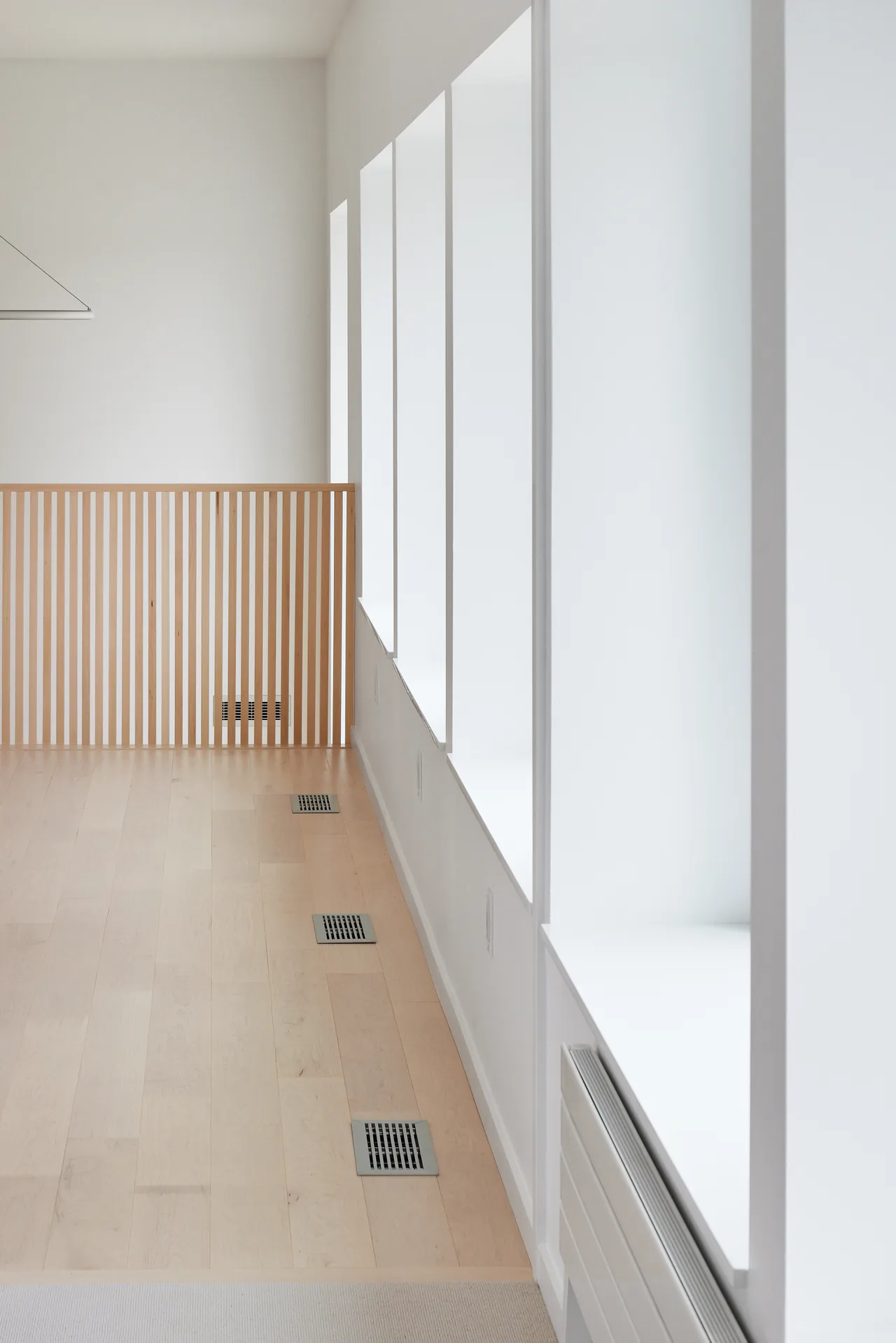 A light wood floor hallway features vertical wood slat railing and large window openings with white frames along one side.