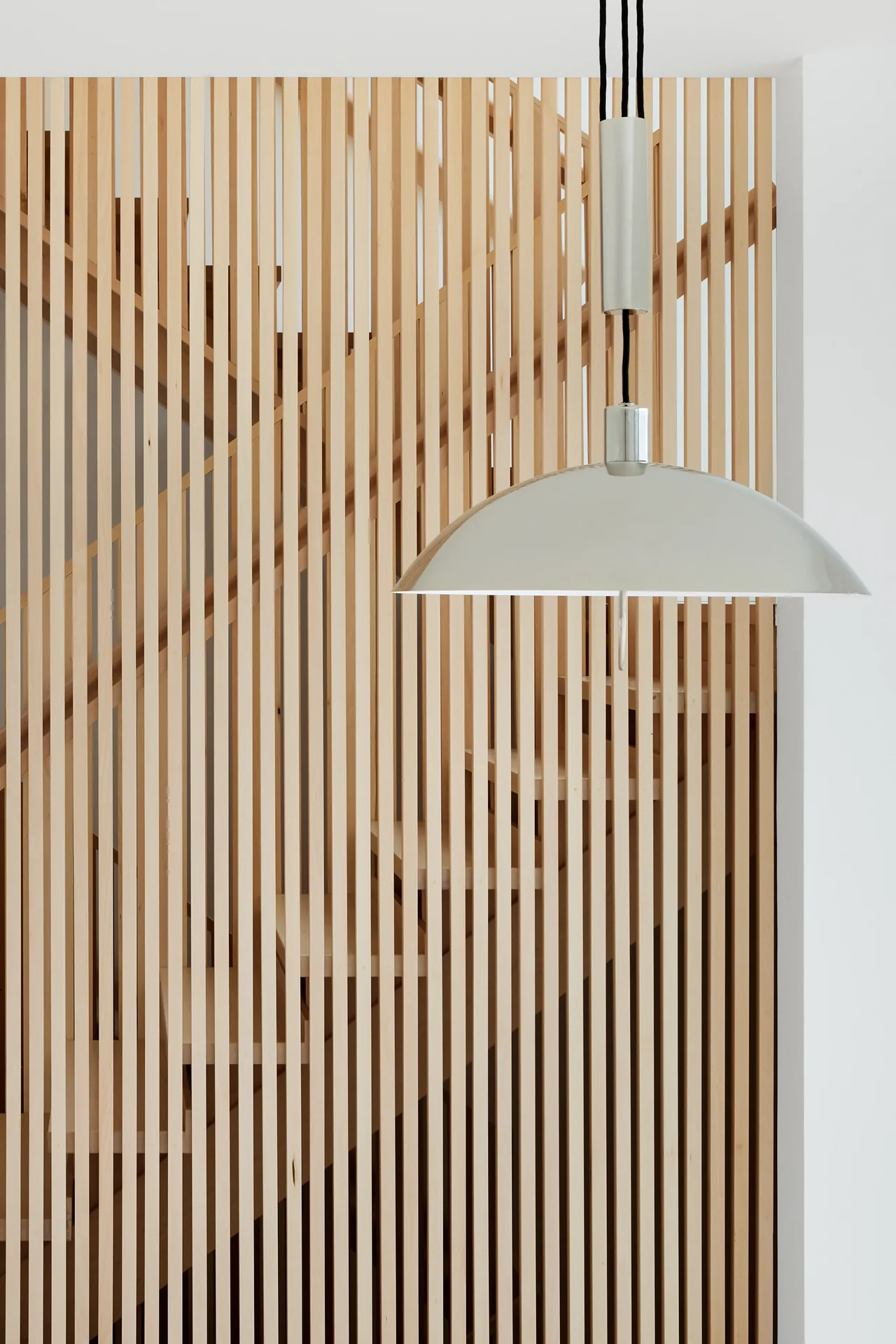 Vertical wooden slats form a screen around a modern staircase, complemented by a minimalist dome pendant light.
