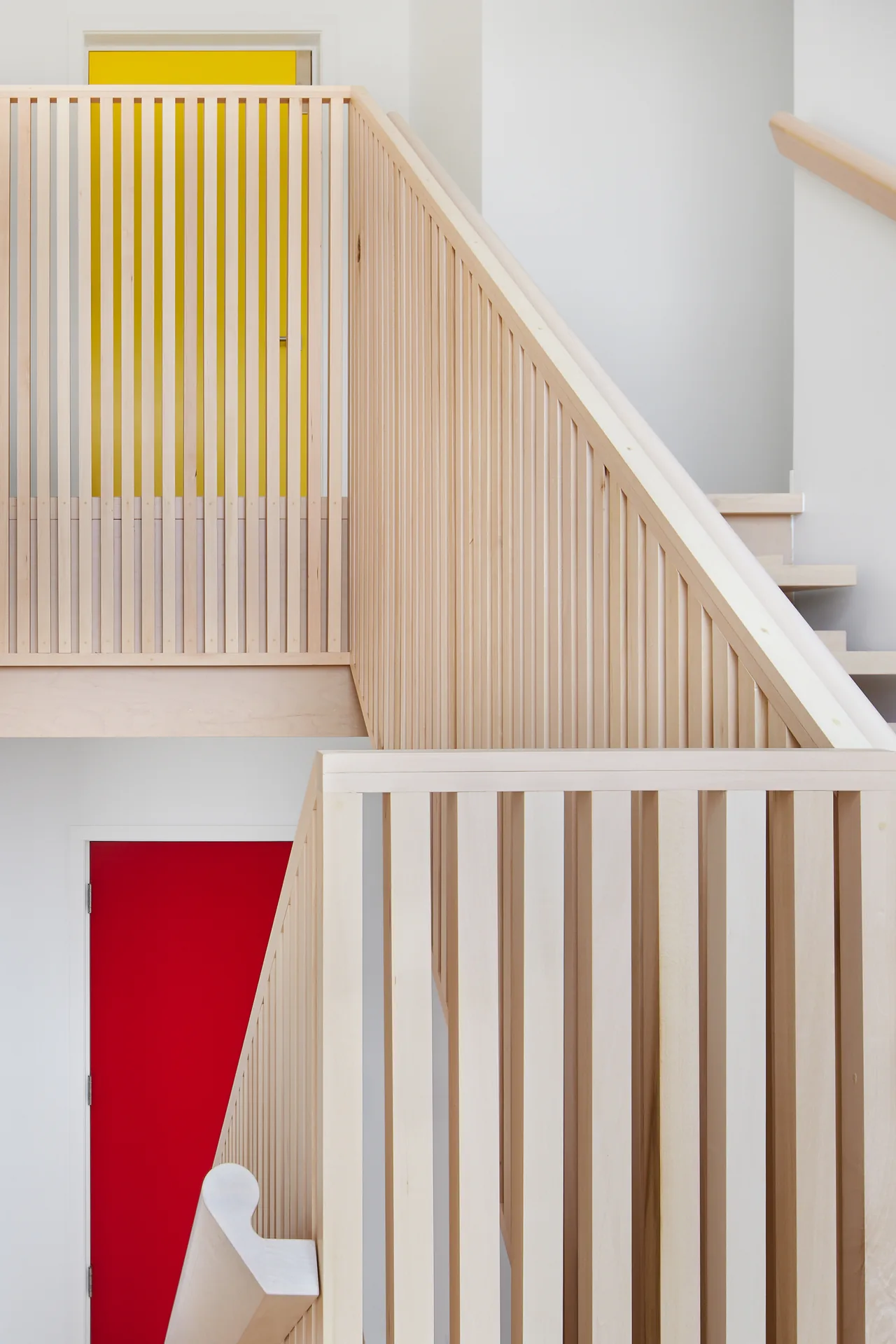 Minimalist staircase with vertical wood slat railing next to red and yellow doors.