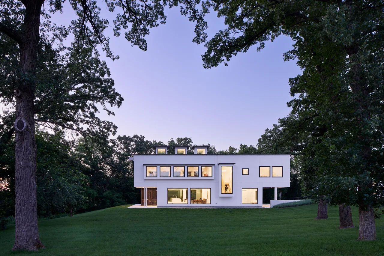 Bauhaus Farm features cubic white volumes with black window frames in a grassy setting at evening light.
