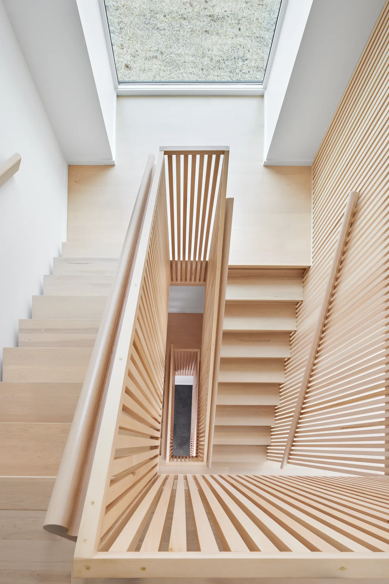 Light wood staircase features vertical slatted railings and a skylight bringing natural light into the stairwell.