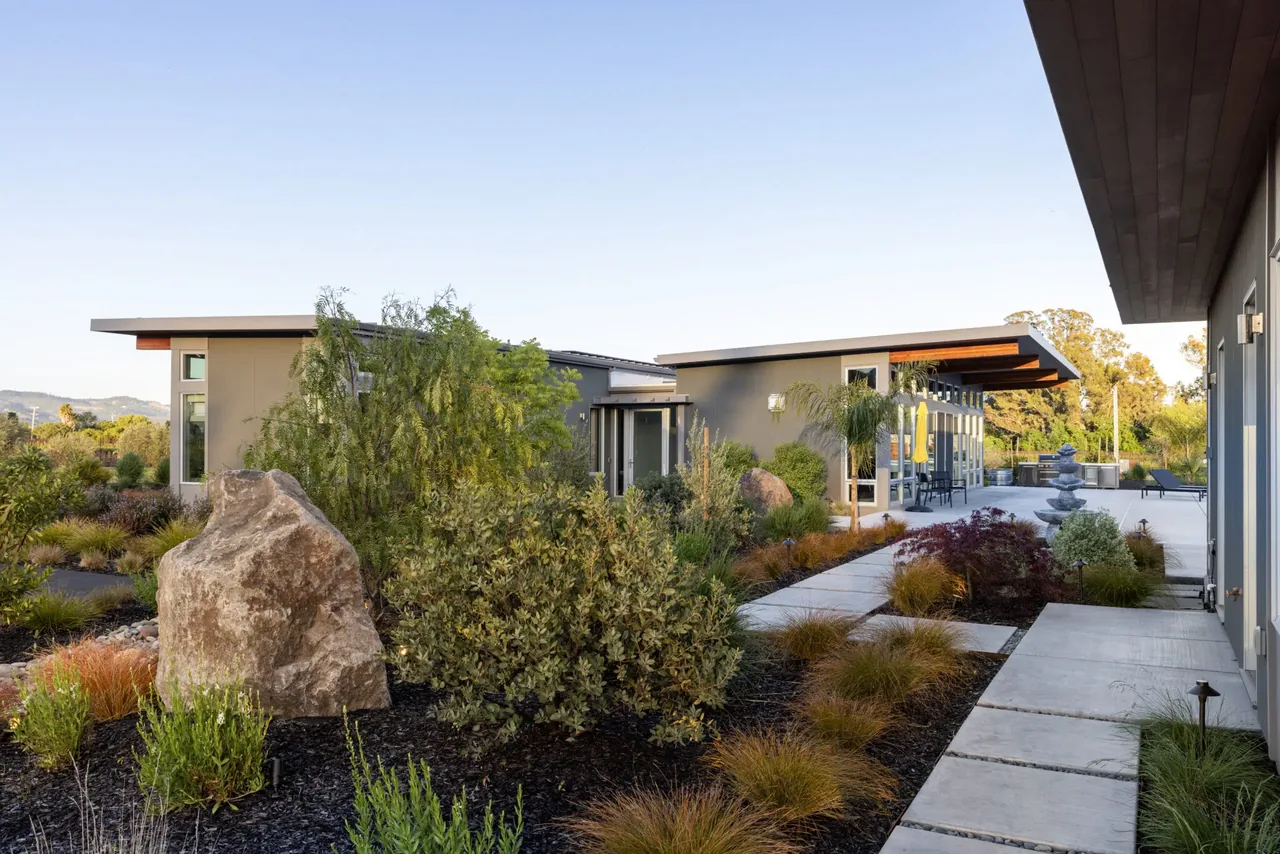Modern residential buildings with landscaped garden beds featuring ornamental grasses and large rocks.