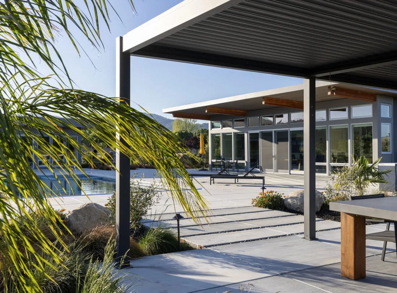 Modern house exterior with large windows and covered patio space overlooking a swimming pool and garden.