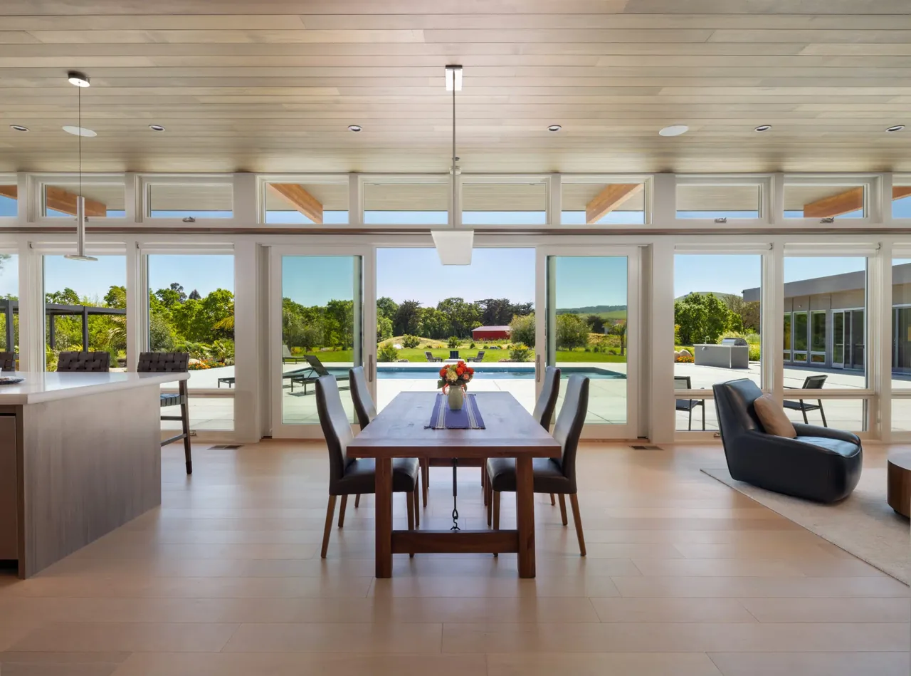 Dining area with wooden table and dark chairs opening to a pool and landscaped garden in Sonoma project.