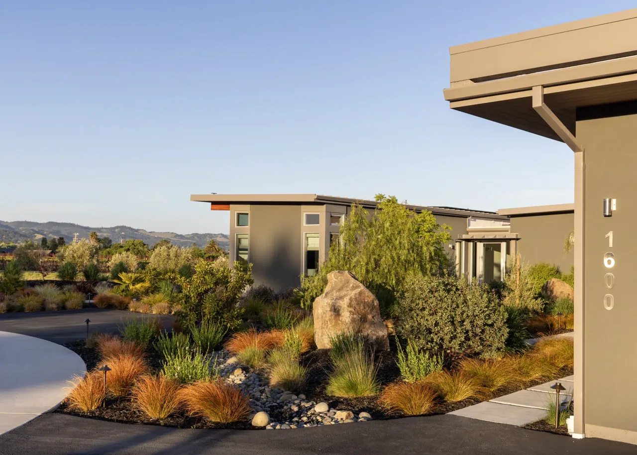 Exterior front of a modern home with landscaping featuring ornamental grasses and large rocks.