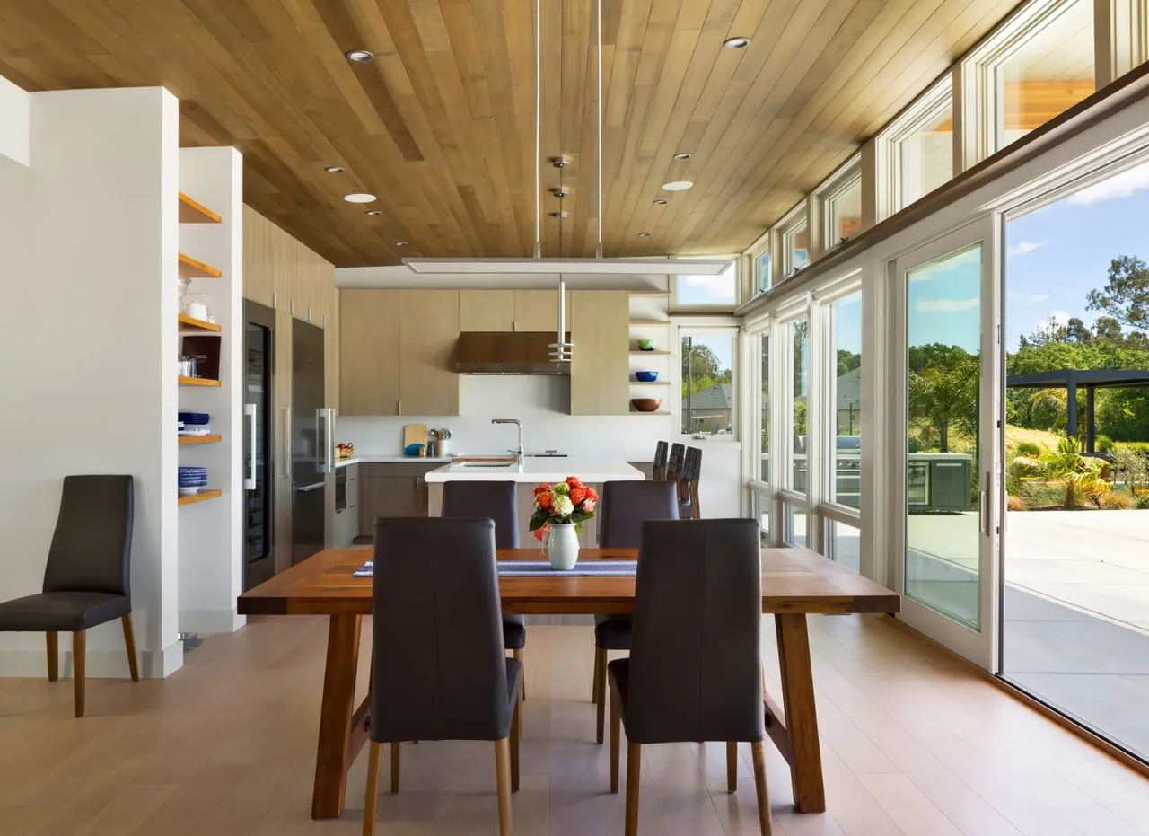 Dining and kitchen area with wood ceiling, large glass windows, and sliding doors leading to a patio in Sonoma project.
