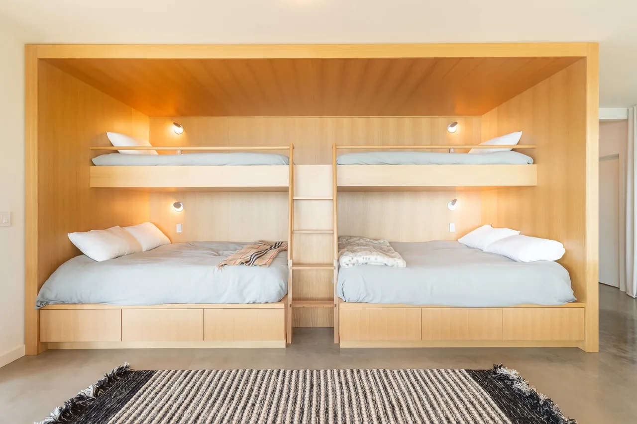 Built-in wooden bunk beds with integrated ladders and reading lights in the Otter Cove House bedroom.