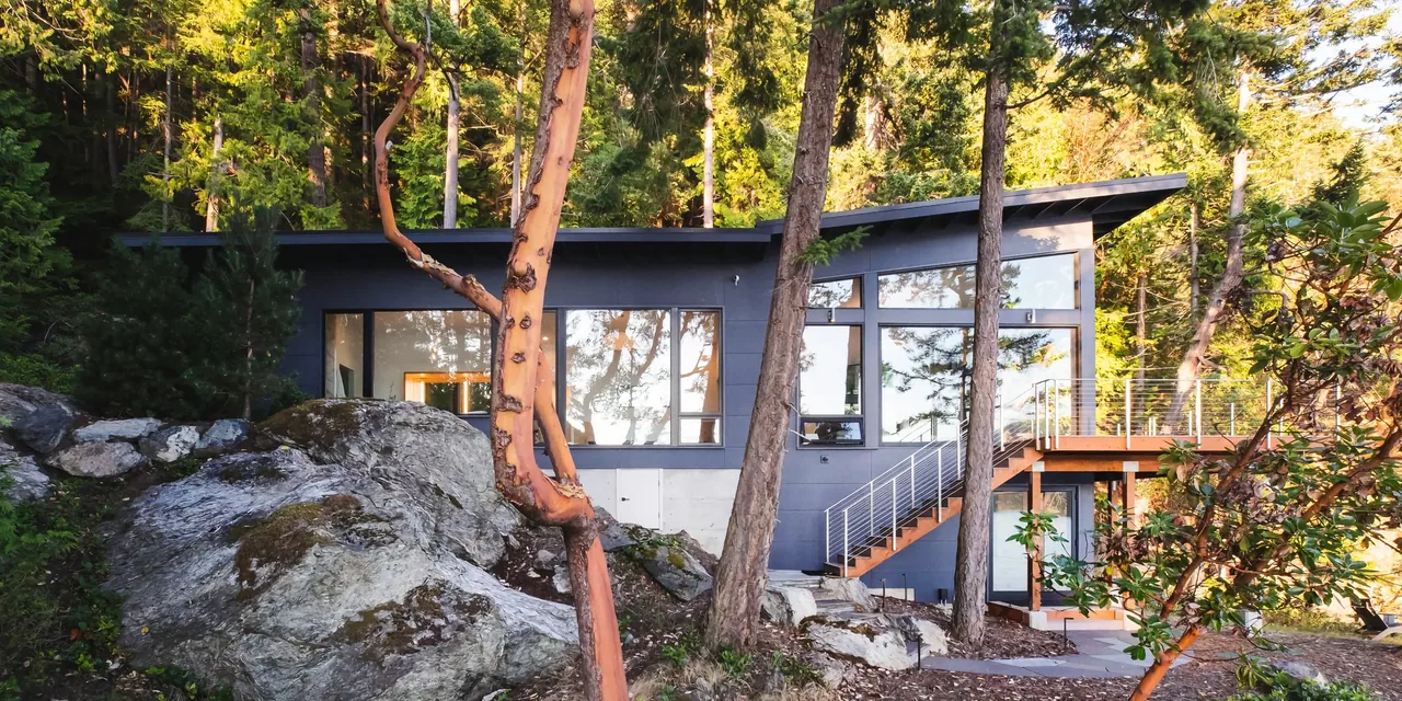 The Otter Cove House by Stoltz Kau Architects features a shed roof and large window walls that blend into the wooded landscape.