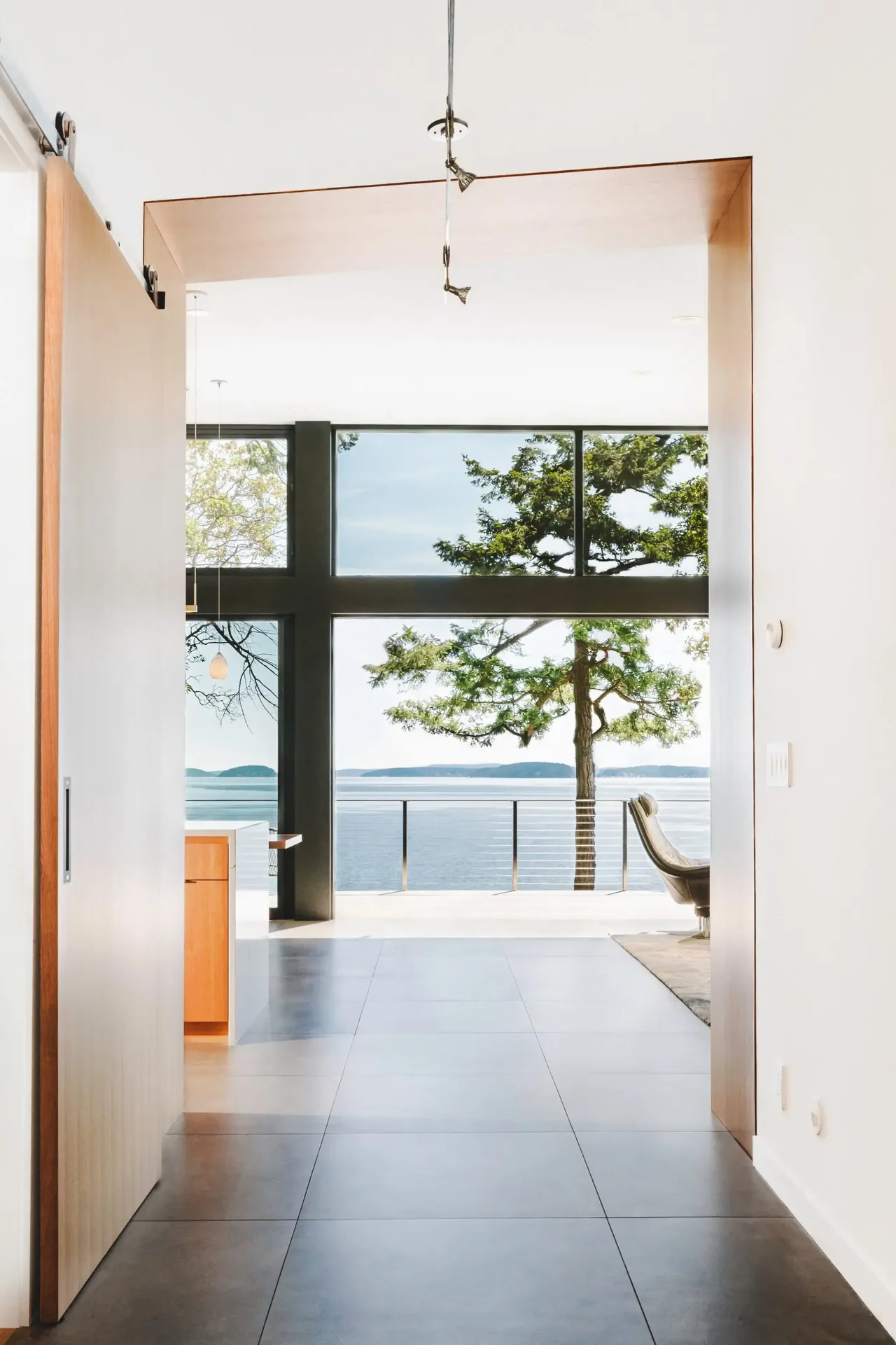 Hallway view leading to floor-to-ceiling glazing with a waterfront and tree view at Otter Cove House.