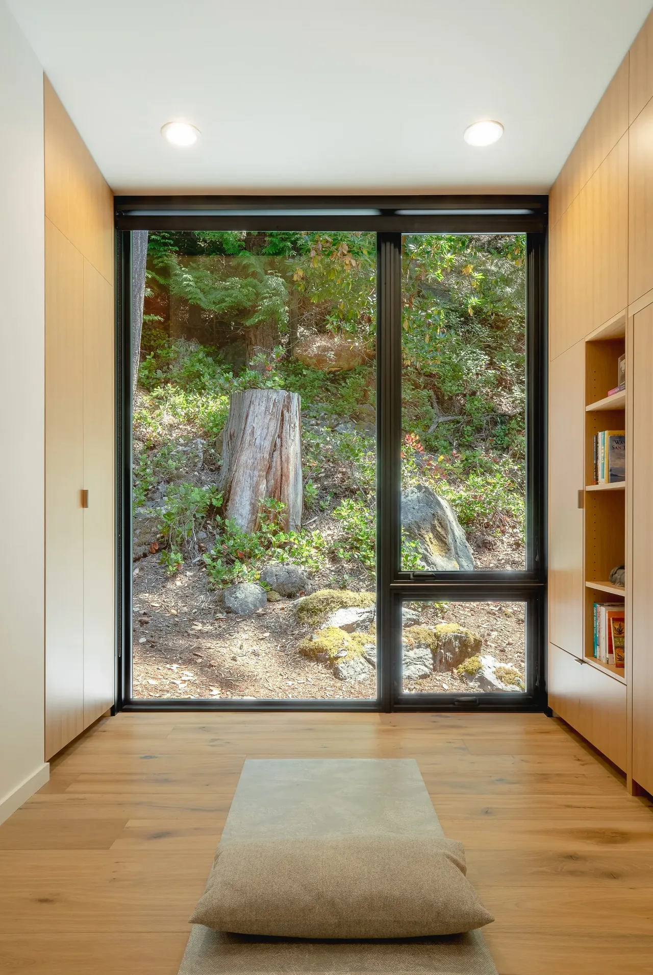 Calm room featuring built-in wood storage and a large black-framed window looking out to nature at Otter Cove House.