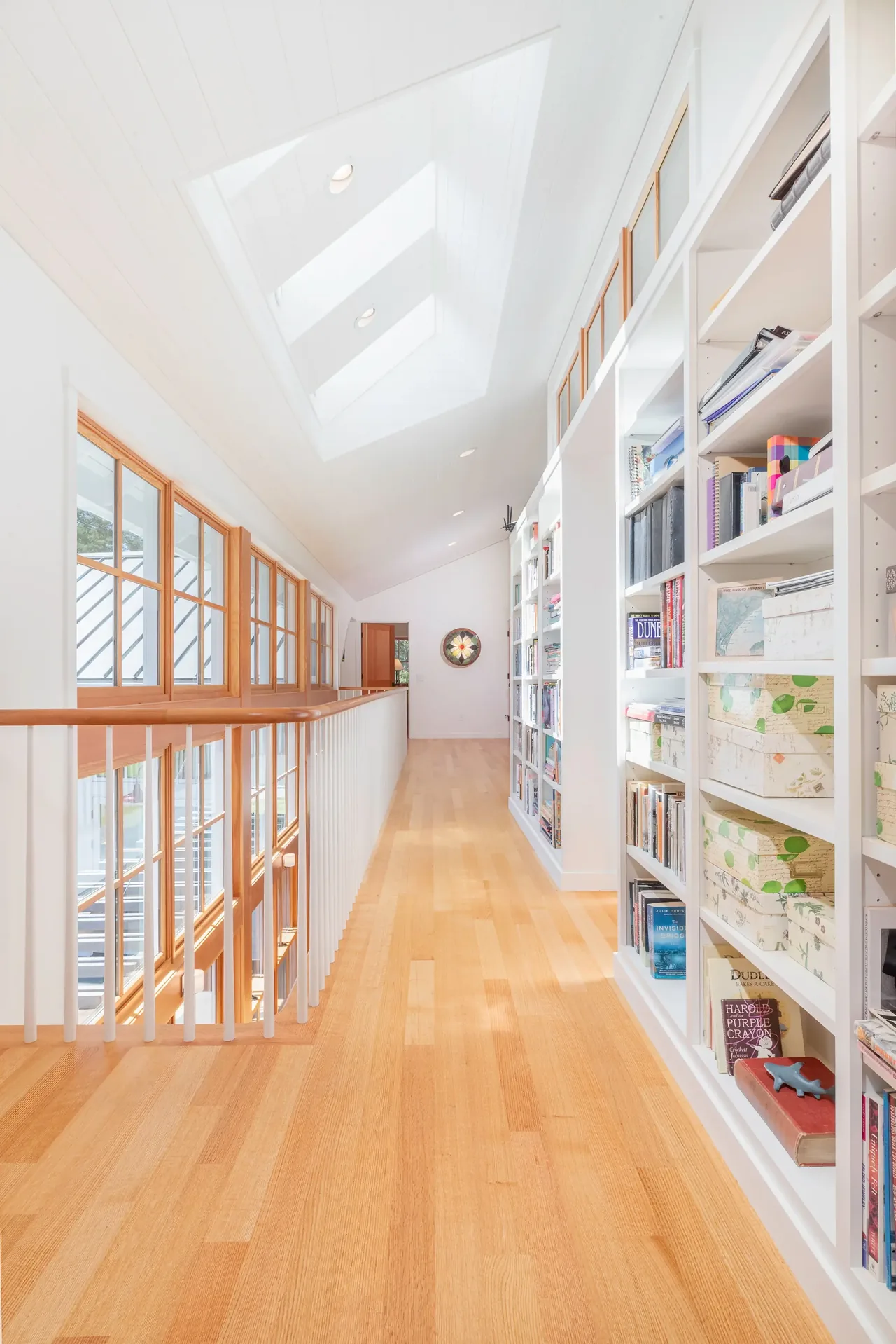 A long hallway featuring built-in bookshelves, wood flooring, and skylights above.