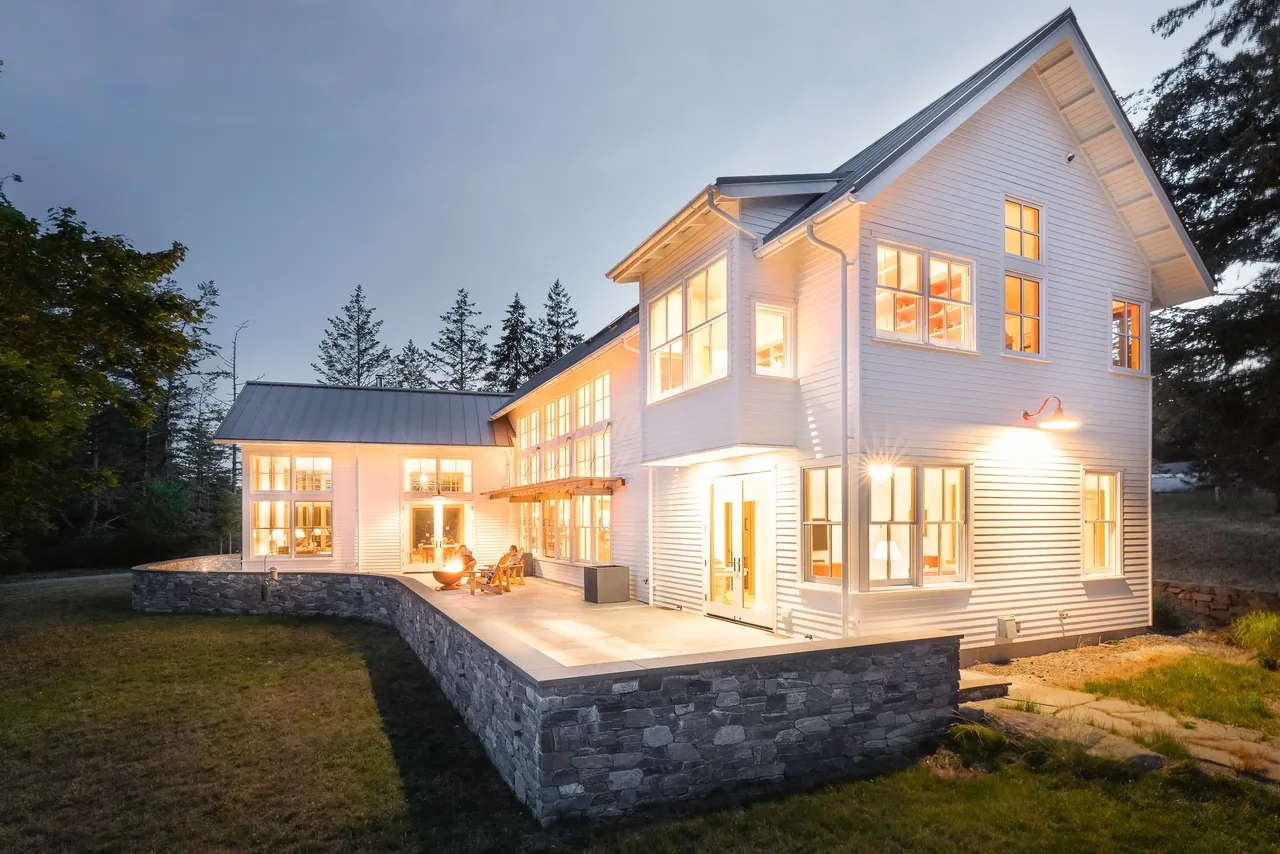 MAP CORNER project by Stoltz Kau Architects features a white wood-sided house with a stone retaining wall patio exterior.