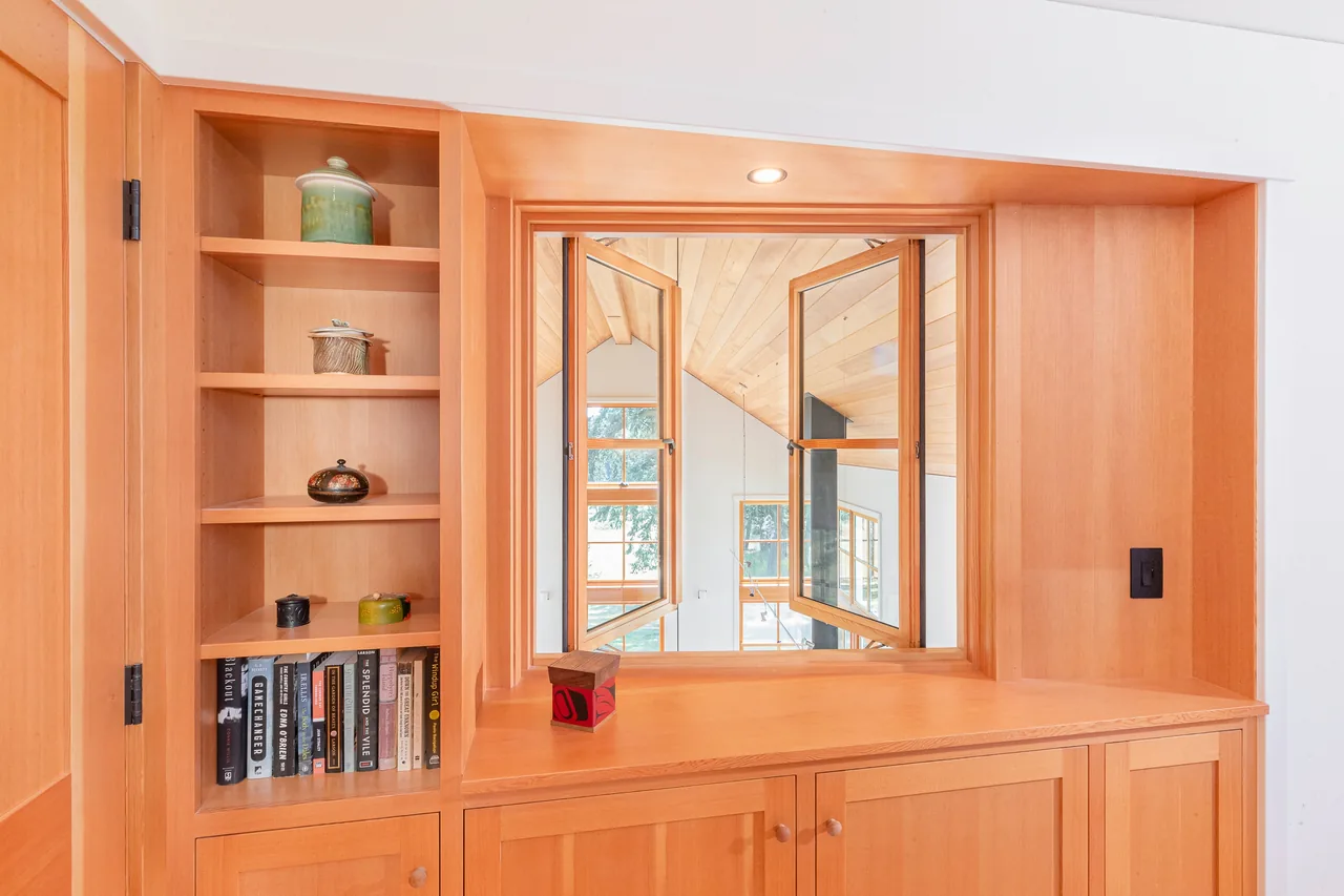 Open wood-framed double casement window set in custom wood cabinetry with shelves and books.