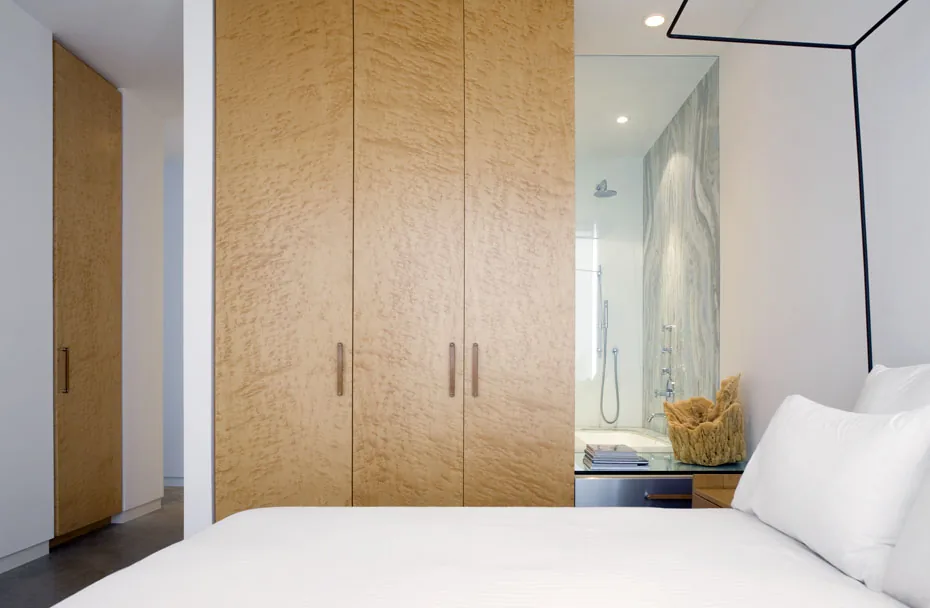 This bedroom features light wood closets and an adjacent bathroom visible through a large glass partition.