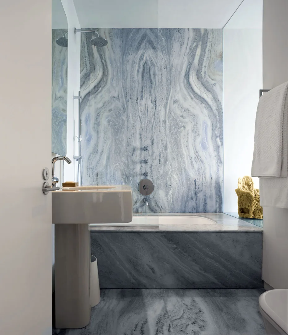 Bathroom featuring extensive gray marble cladding on walls and floors with a pedestal sink and built-in bathtub.